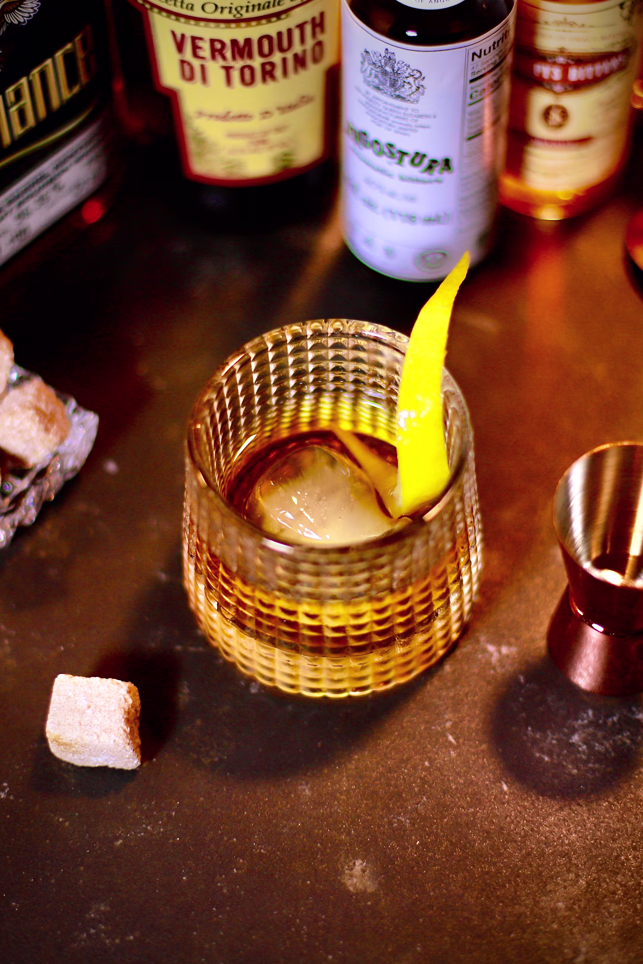 Classic Old Fashioned cocktail with a large clear ice cube and orange peel garnish in a heavy tumbler.